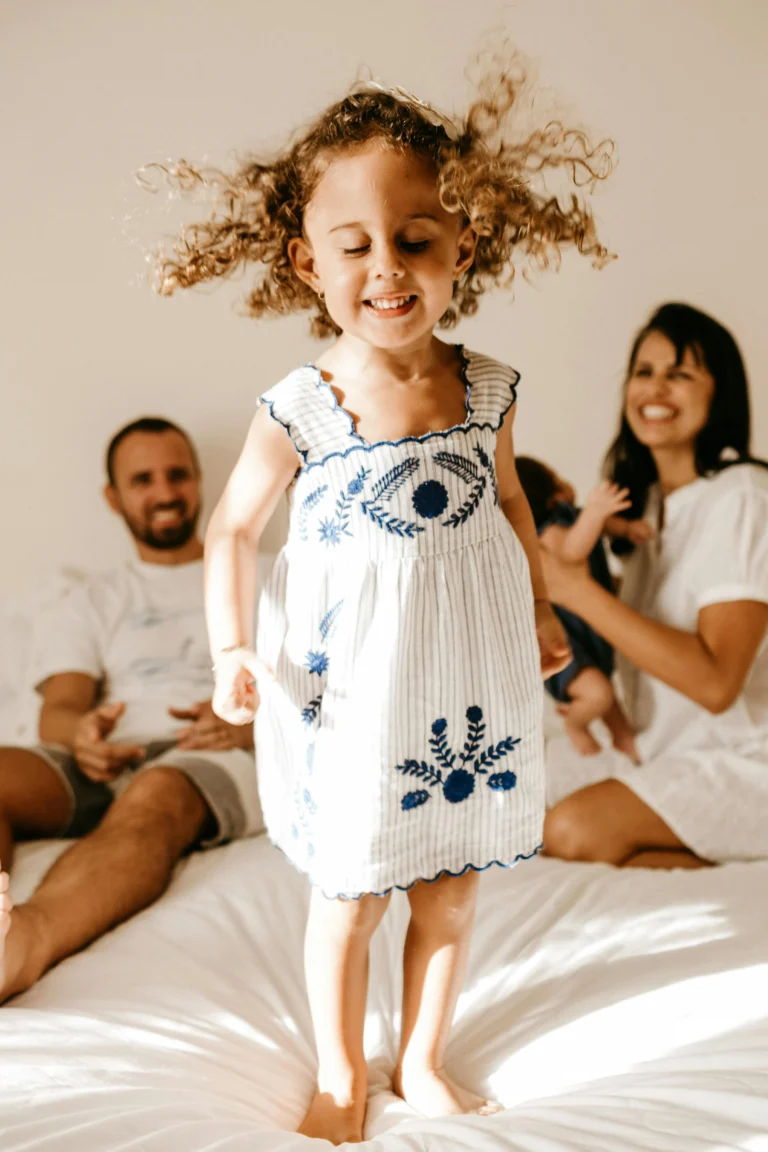 Glückliches Mädchen hüpfend auf dem Elternbett zusammen mit der Familie